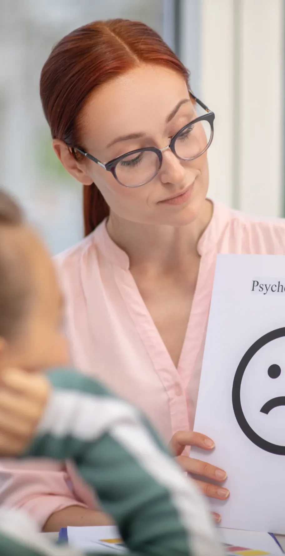 psychological test featured image A woman in a pink blouse holds a sign labeled "Psychological test" featuring a sad face, while a girl listens attentively.